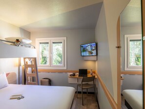Habitación de hotel con literas, un escritorio con una computadora portátil, un televisor montado en la pared y una ventana con vista a árboles.