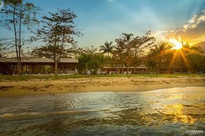 A beachfront property with a sandy beach, a body of water, and a building with a tiled roof. - Hostel Canto Caiçara (Paraty)