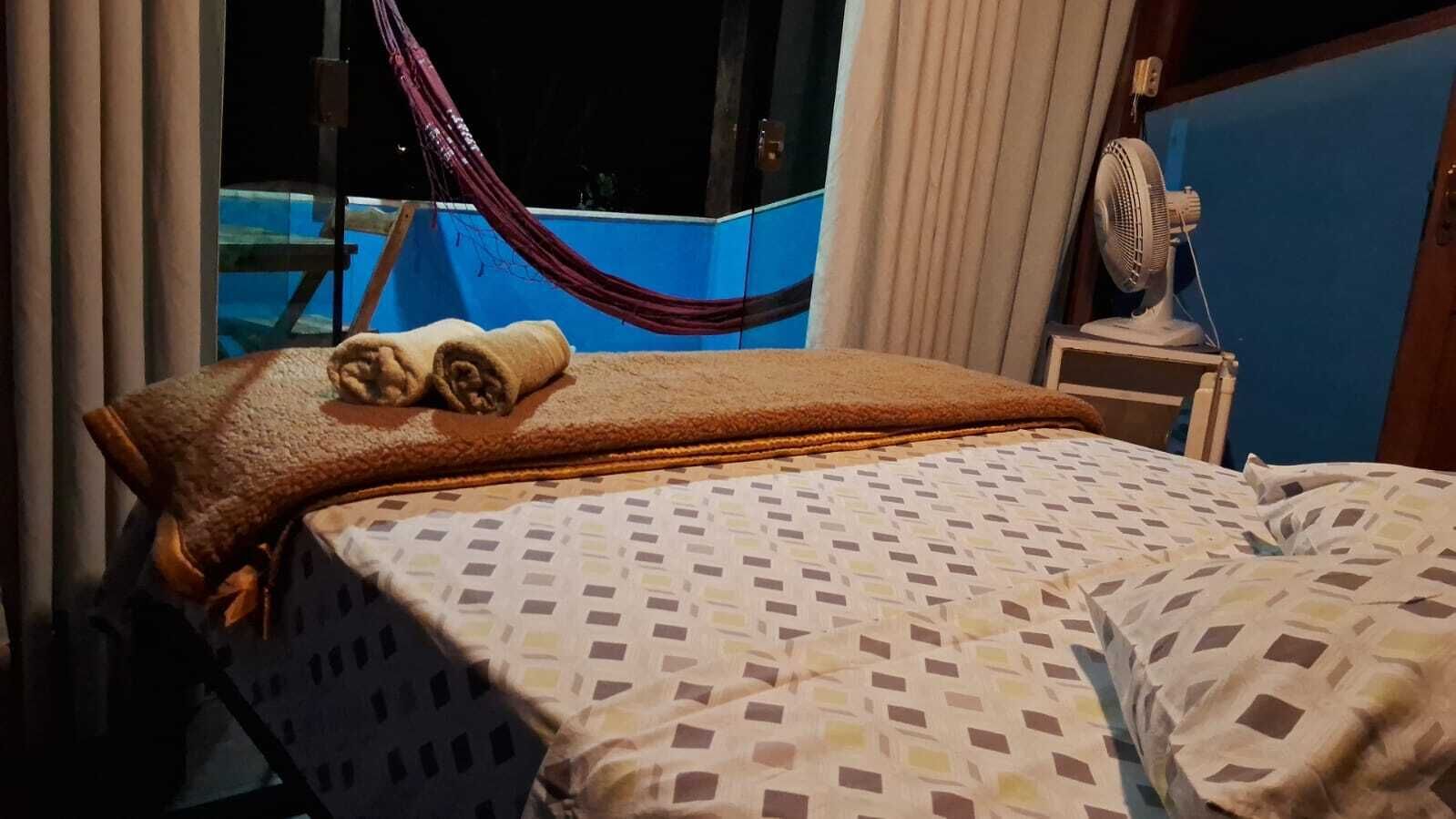 Ein Bett mit einem gemusterten Überwurf, ein zusammengerolltes Handtuch und ein Standventilator.