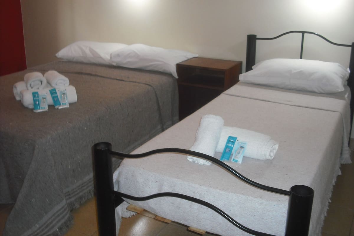 Two single beds with white linens, a wooden nightstand, and a small table with toiletries.