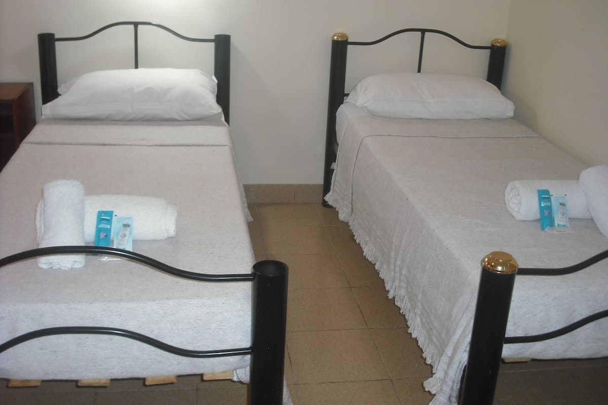 Two single beds with white linens and towels, a wooden nightstand, and a tiled floor.