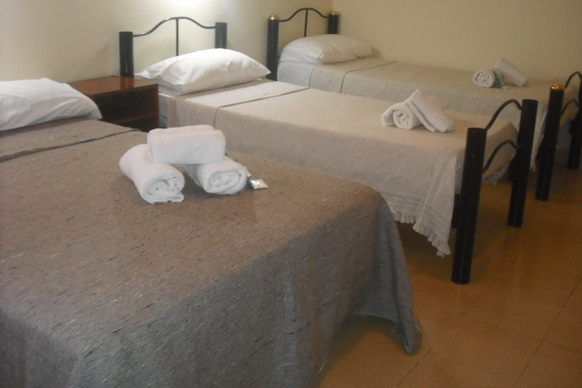 A hotel room with three single beds, each with a neatly folded towel and a pillow.