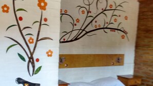 A bedroom with a bed, a nightstand, and a wall with floral artwork. - Nuevo Raices Apart (Puerto Iguazú)