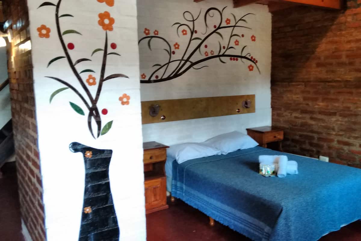 A bedroom with a bed, wooden headboard, and a brick wall.