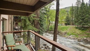 Eine Holzterrasse mit einem grünen Sitzkissen und einem kleinen Tisch, mit Blick auf einen Fluss und einen dichten Wald.