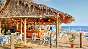 A beachside bar with thatched roof, outdoor seating, and a view of the sea.