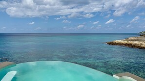 A clear blue pool with a view of the ocean and a rocky shoreline.