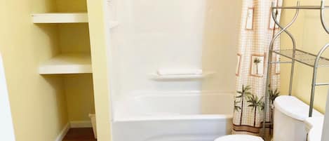 A bathroom with a bathtub, toilet, and shelves.