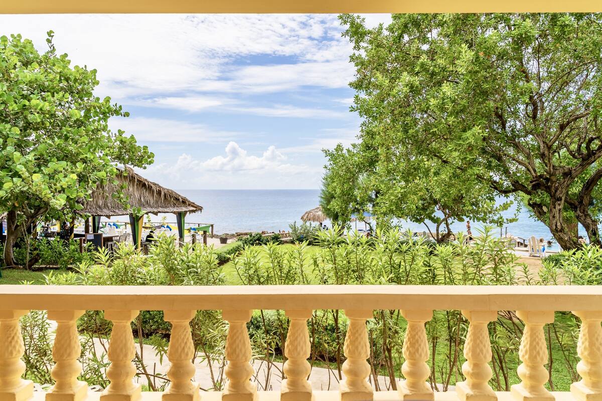A view of a beachside resort with a thatched-roof structure, lush greenery, and a clear view of the sea.