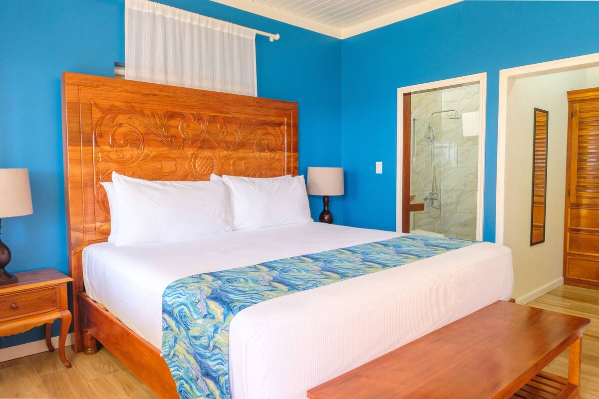 A bedroom with a wooden headboard, a large bed with white bedding, a bedside table with a lamp, and a bench.