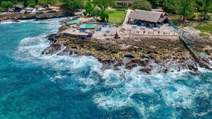 A coastal resort with a pool area, lounge chairs, and a thatched-roof structure.