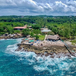 A coastal resort with a pool area, lounge chairs, and a thatched-roof structure.