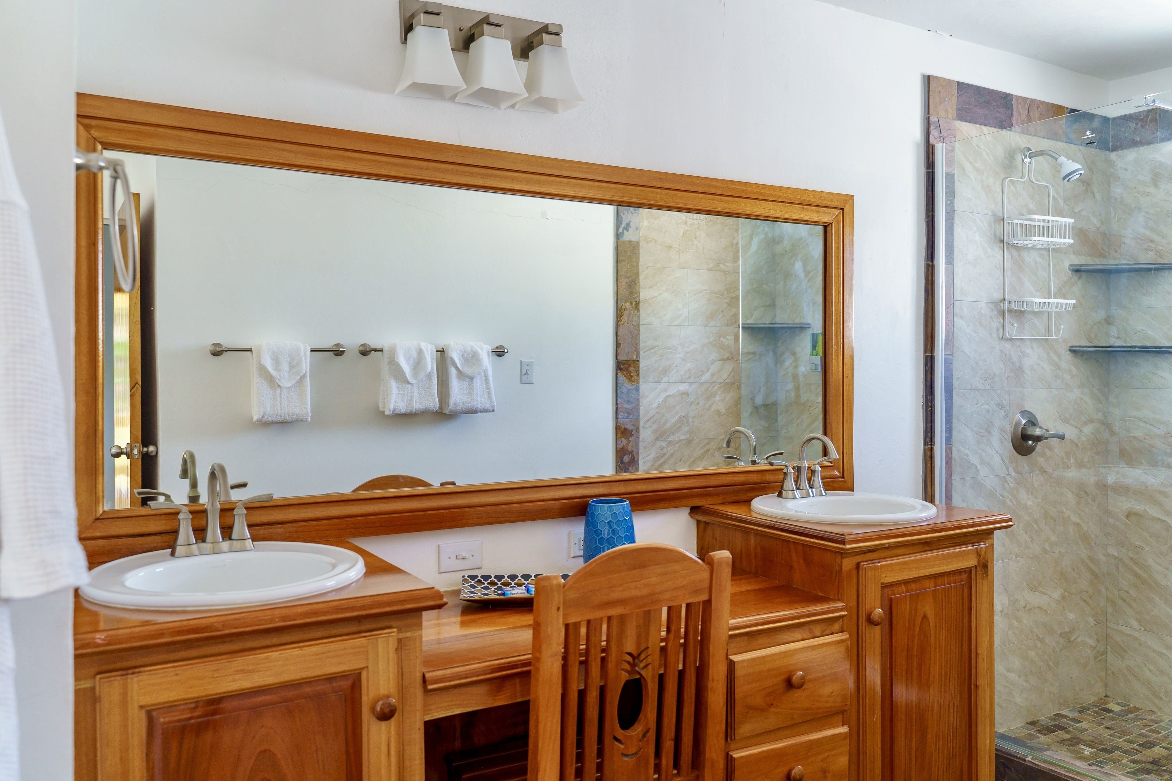 Ein Badezimmer mit zwei Waschbecken, einem großen Spiegel, Holzschränken und einer Duschkabine.