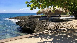 A beach with a thatched-roof hut, a rocky shoreline, and a clear blue sky. - The Westender Inn (Negril)