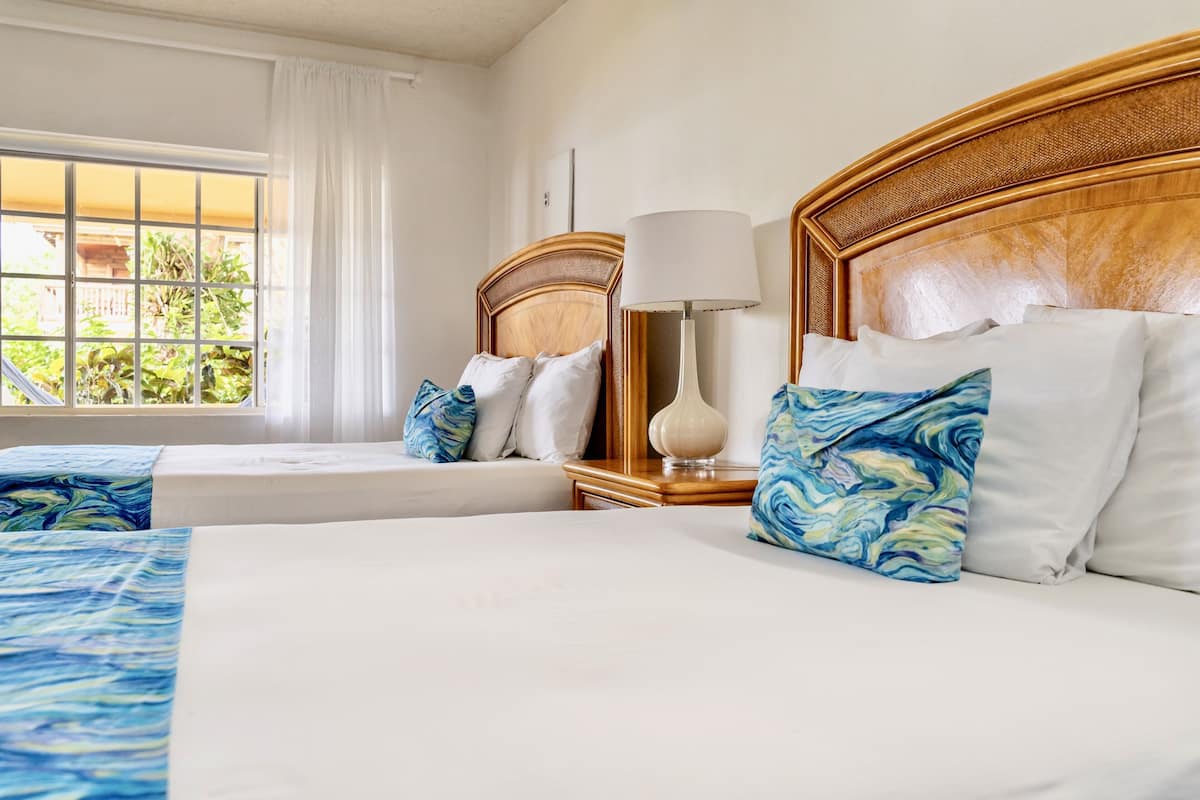 A hotel room with two beds, a nightstand with a lamp, and a window with curtains.