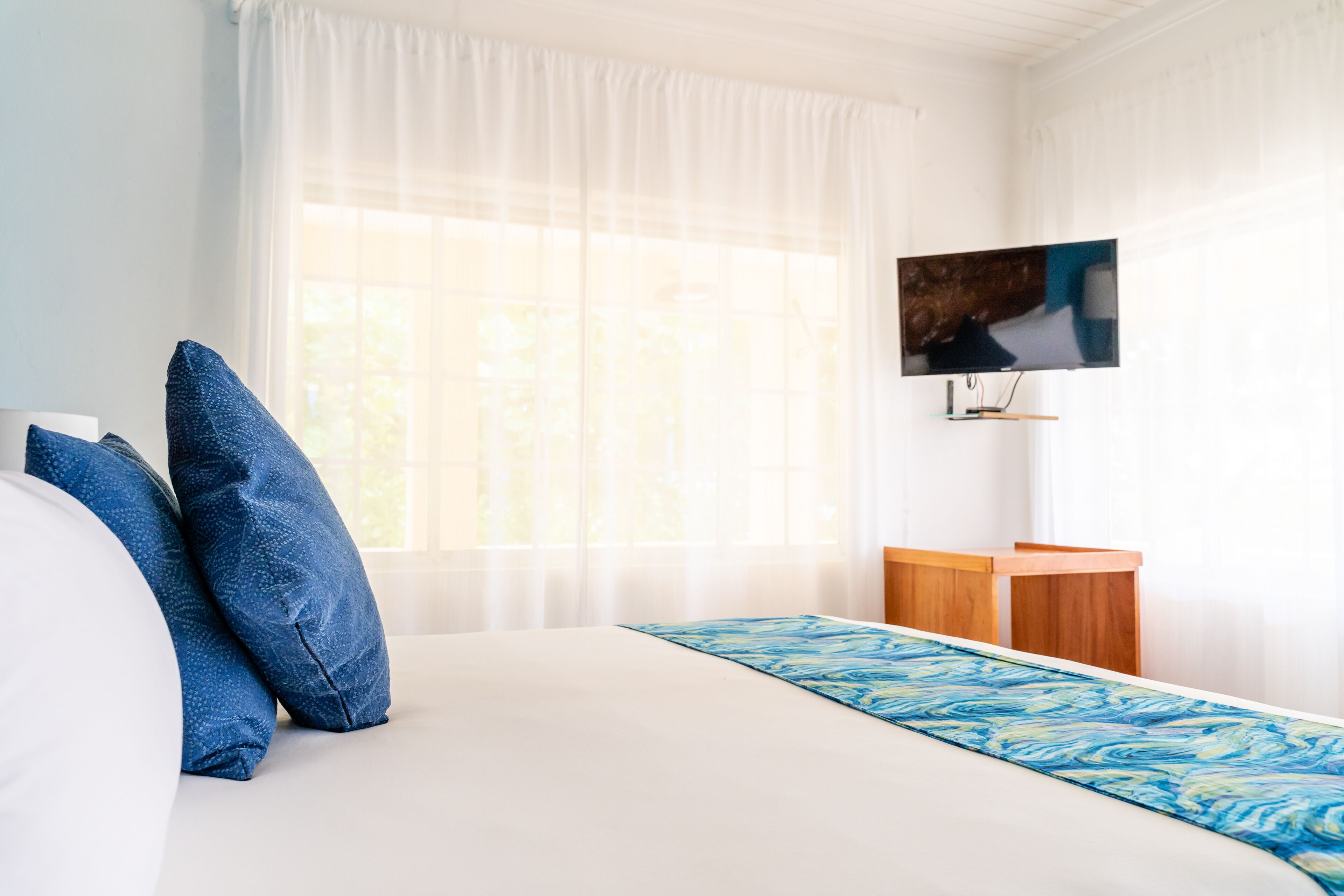 Una habitación de hotel con una cama grande, un televisor montado en la pared y una mesita de noche de madera.