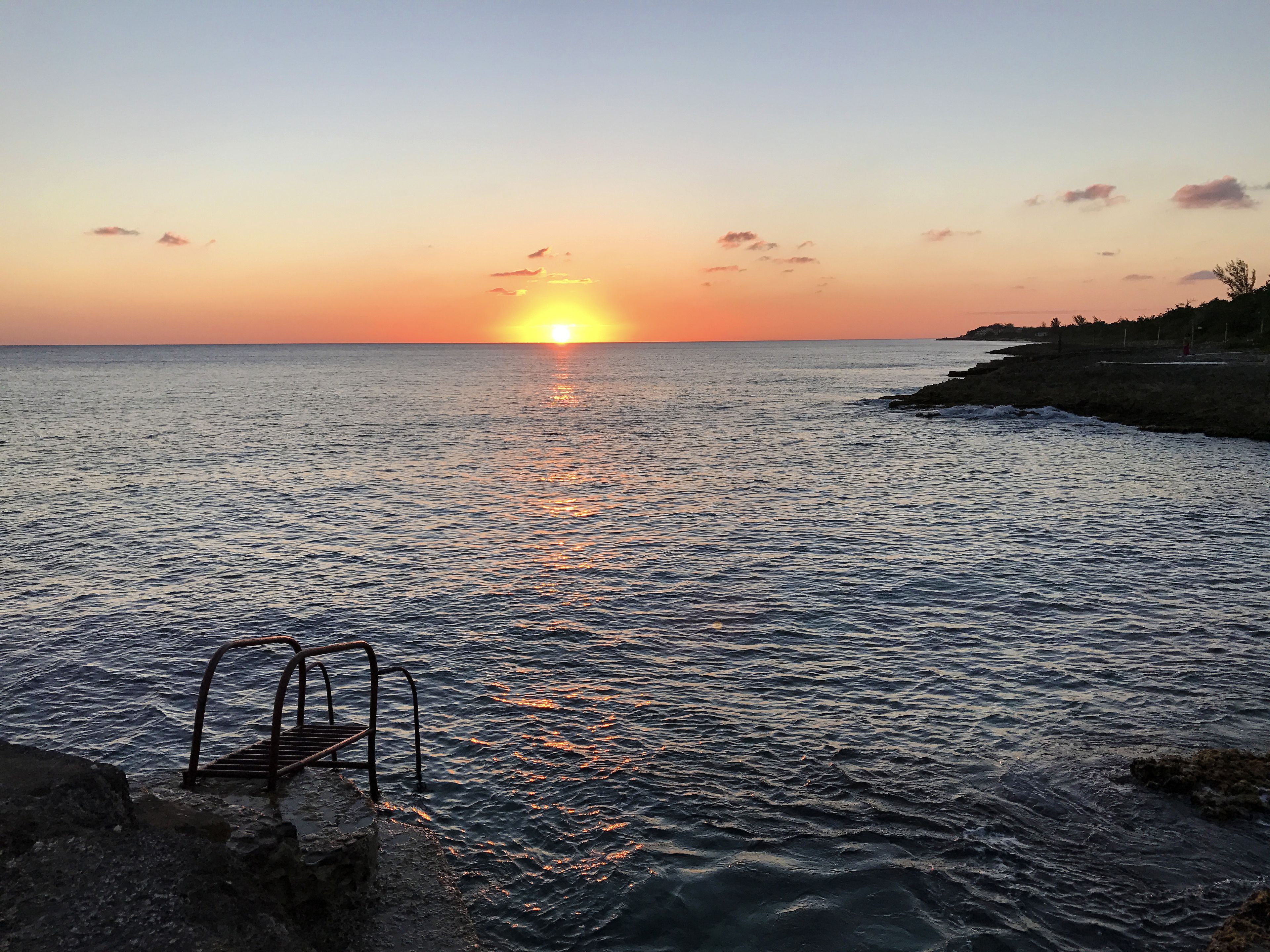 A sunset over a calm sea with a metal ladder leading into the water.
