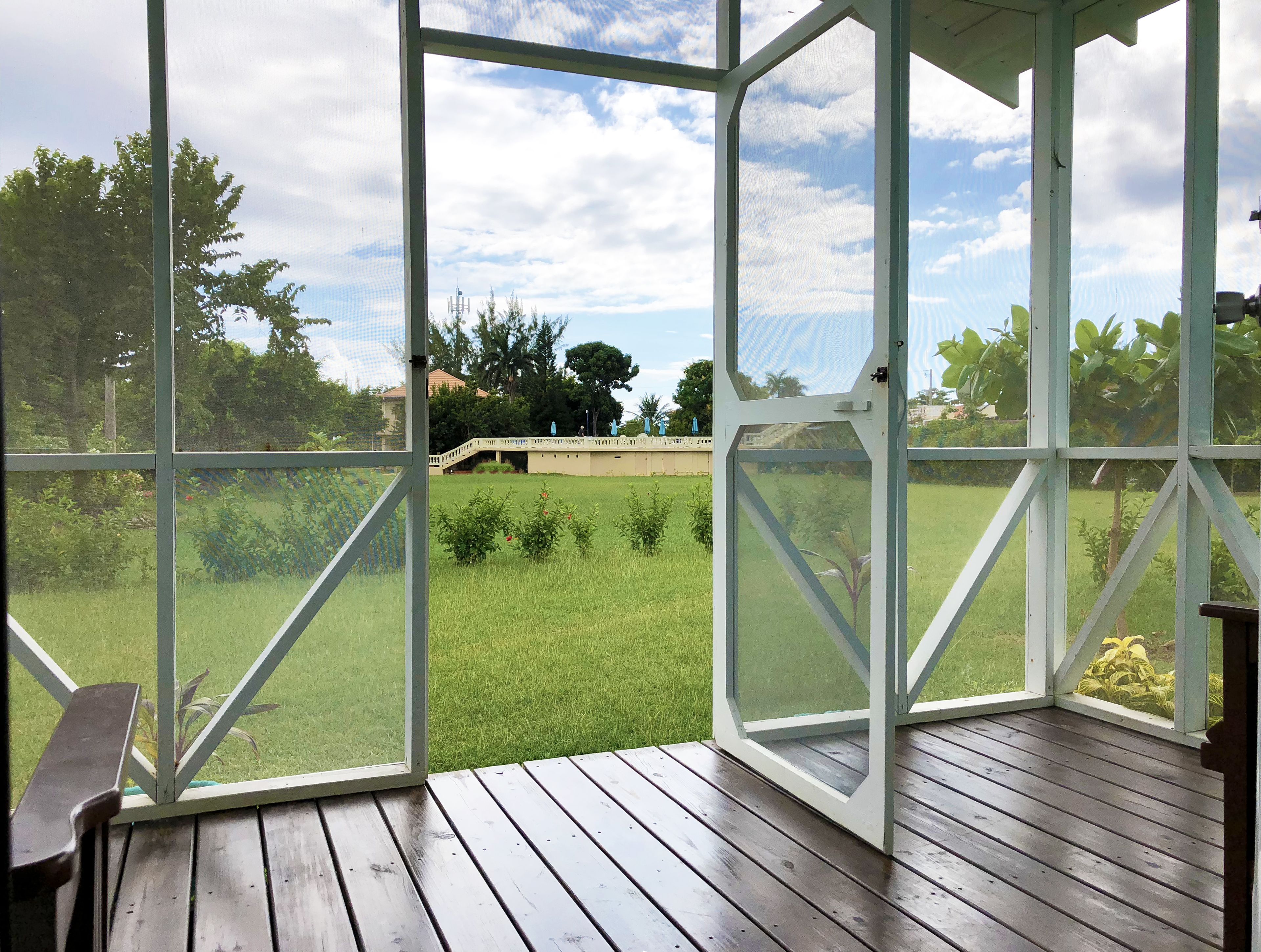 A covered outdoor area with a wooden deck, a view of a grassy field, and a building in the background.