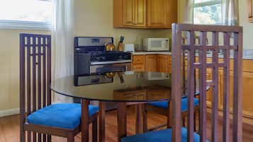 Una cocina con armarios de madera, una estufa a gas, un microondas y una mesa de comedor de vidrio con sillas azules.