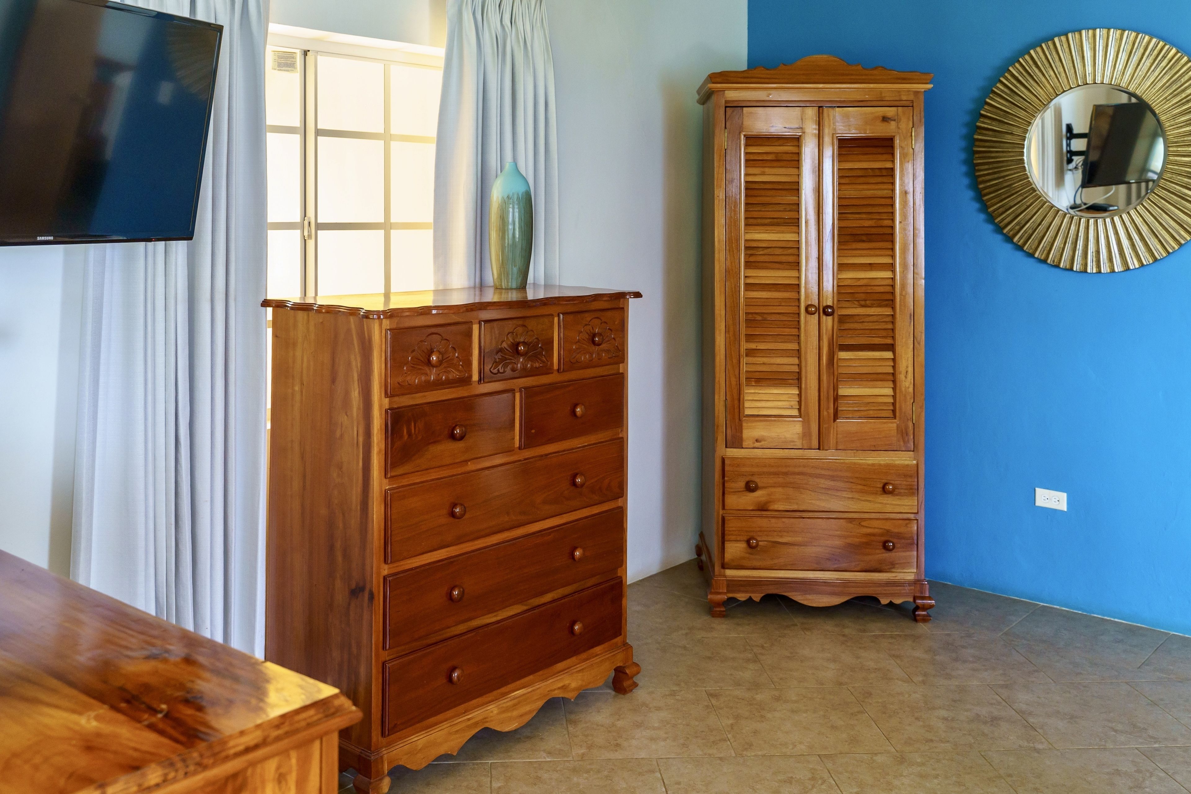 A room with a wooden dresser, a cabinet, a television, and a mirror on the wall.