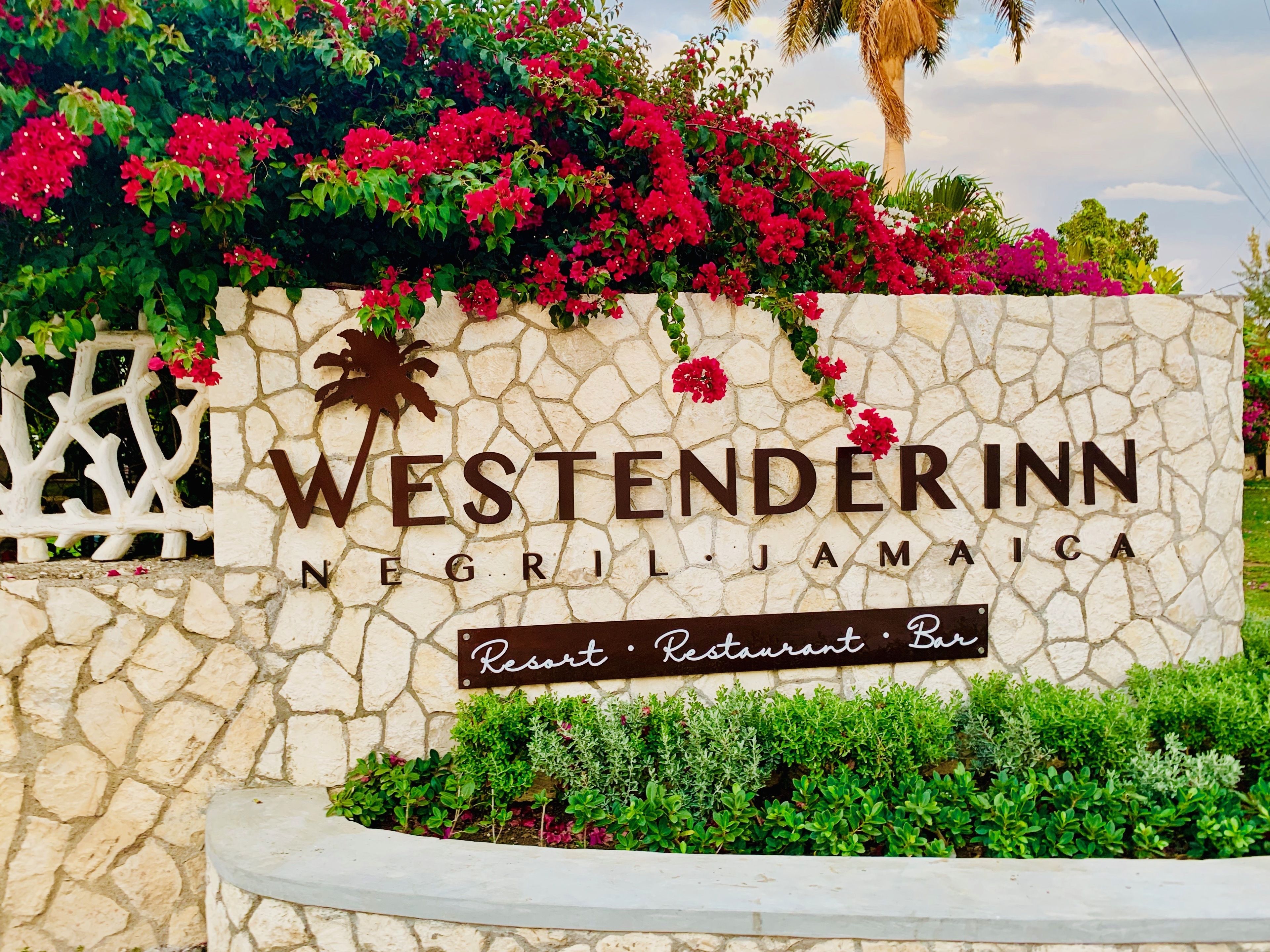 A sign for Westenderinn Resort Restaurant Bar with a stone wall and lush greenery.