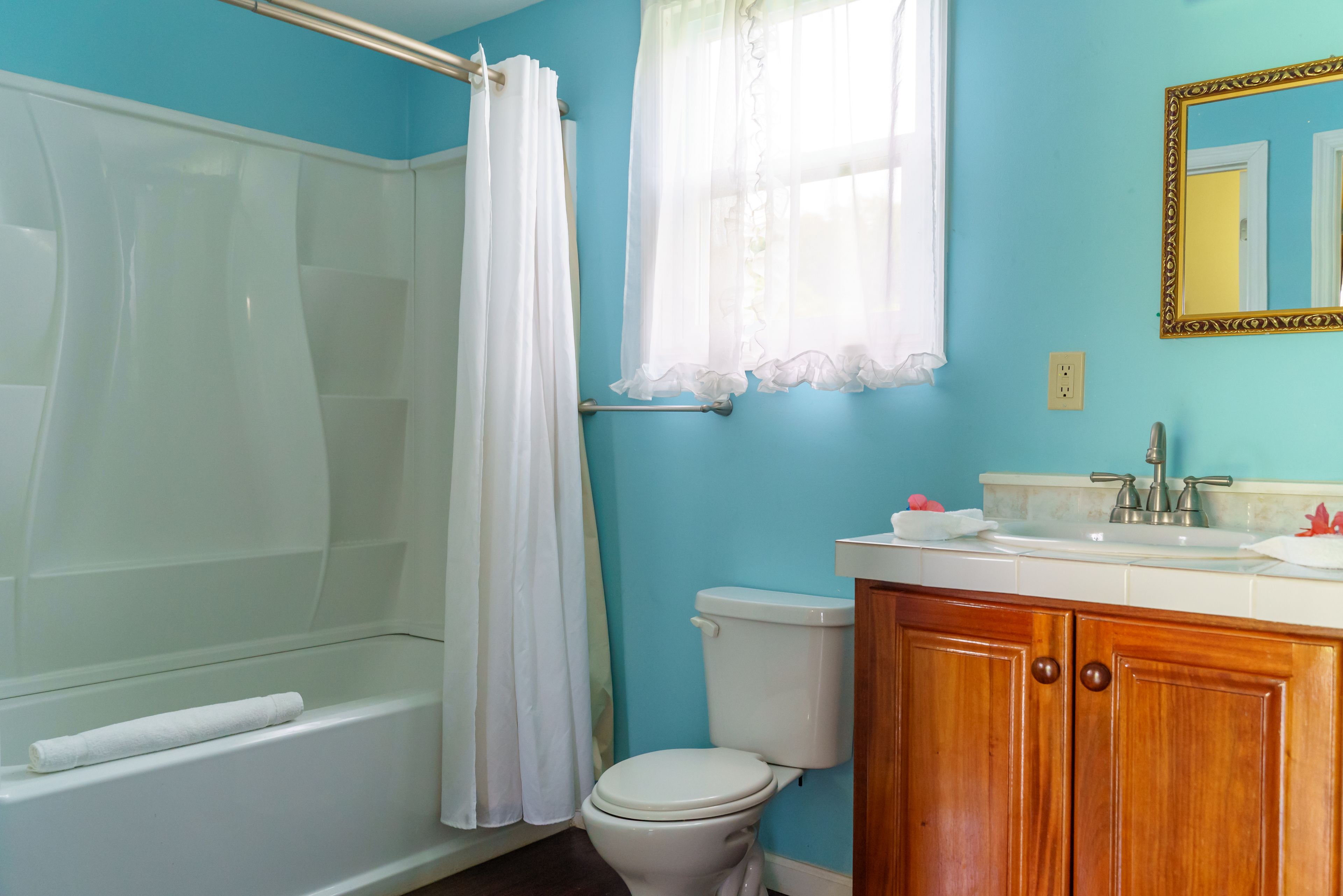 Un baño con bañera, inodoro, tocador y una ventana con cortina.
