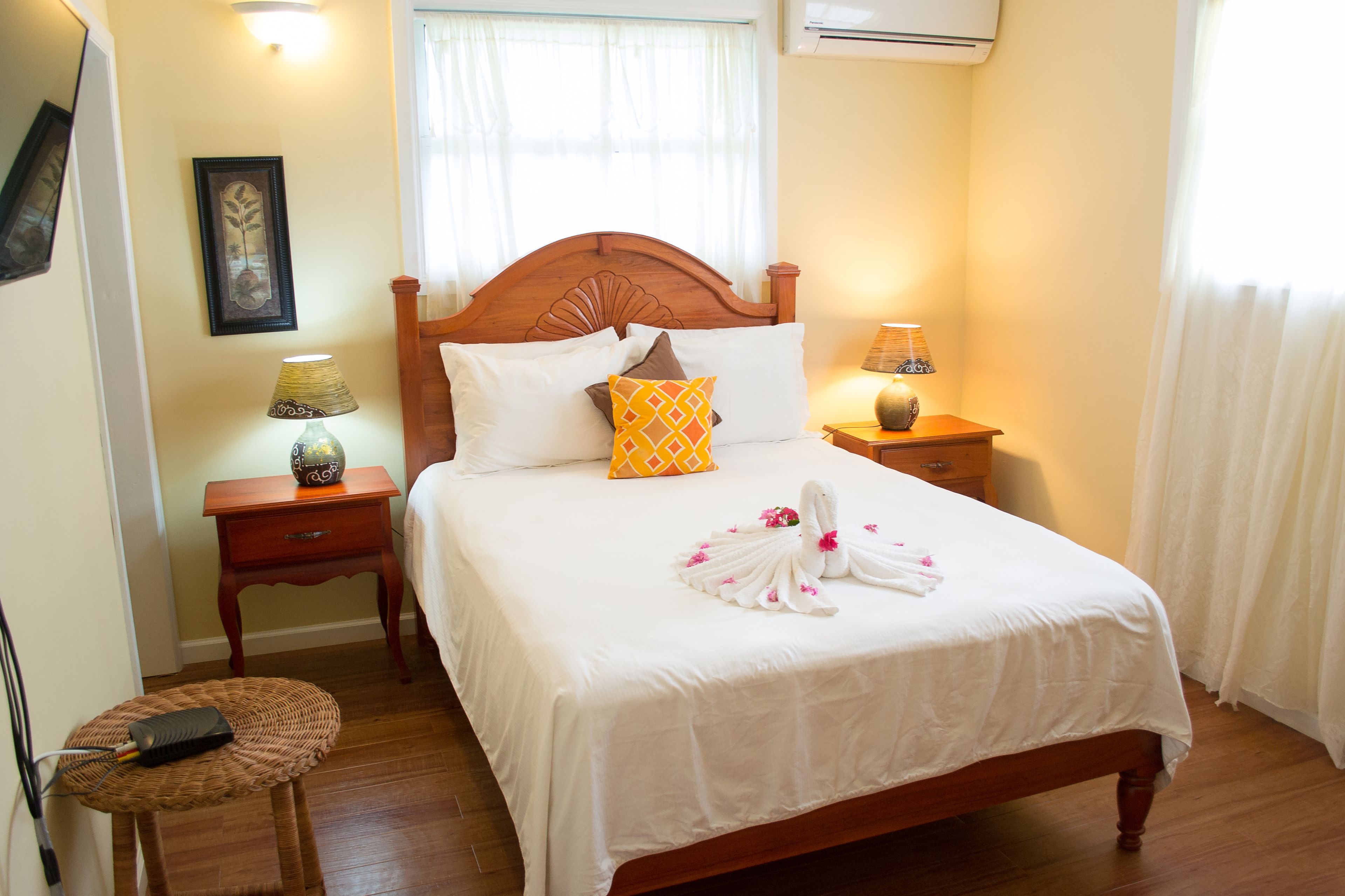 A neatly made bed with a white bedspread, a wooden headboard, and decorative pillows. There is a bedside lamp on the nightstand beside the bed.