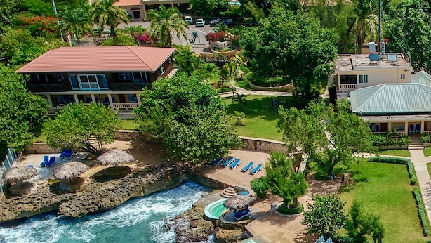 A coastal resort with multiple swimming pools, lounge areas, and a rocky shoreline. - The Westender Inn (Negril)