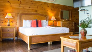 A wooden-paneled room with a bed, two bedside tables with lamps, a dresser, a television, and a mirror.