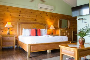 A wooden-paneled room with a bed, two bedside tables with lamps, a dresser, a television, and a mirror.