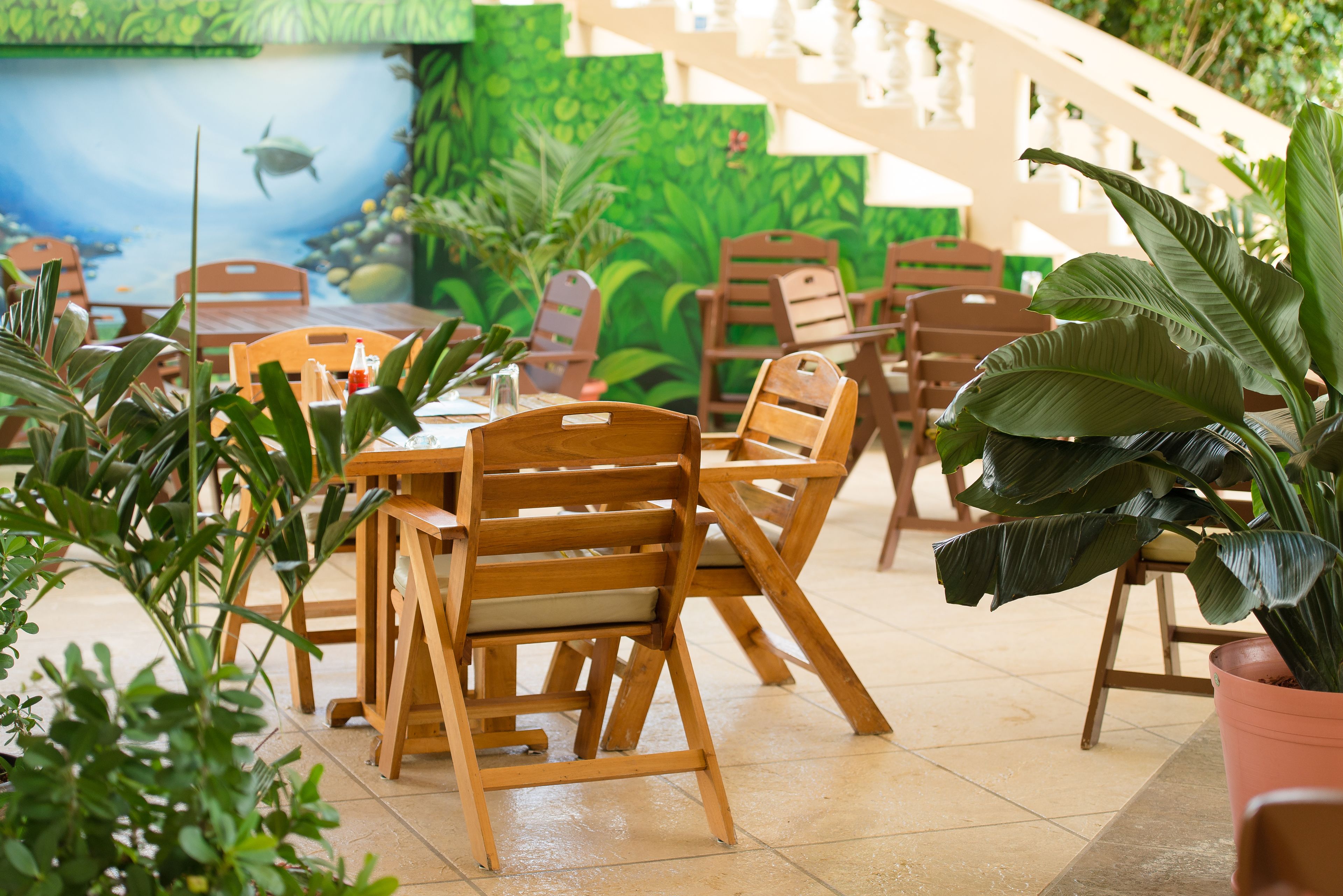 Een restaurant met houten tafels en stoelen, potplanten en een muurschildering van een vis die in het water zwemt.