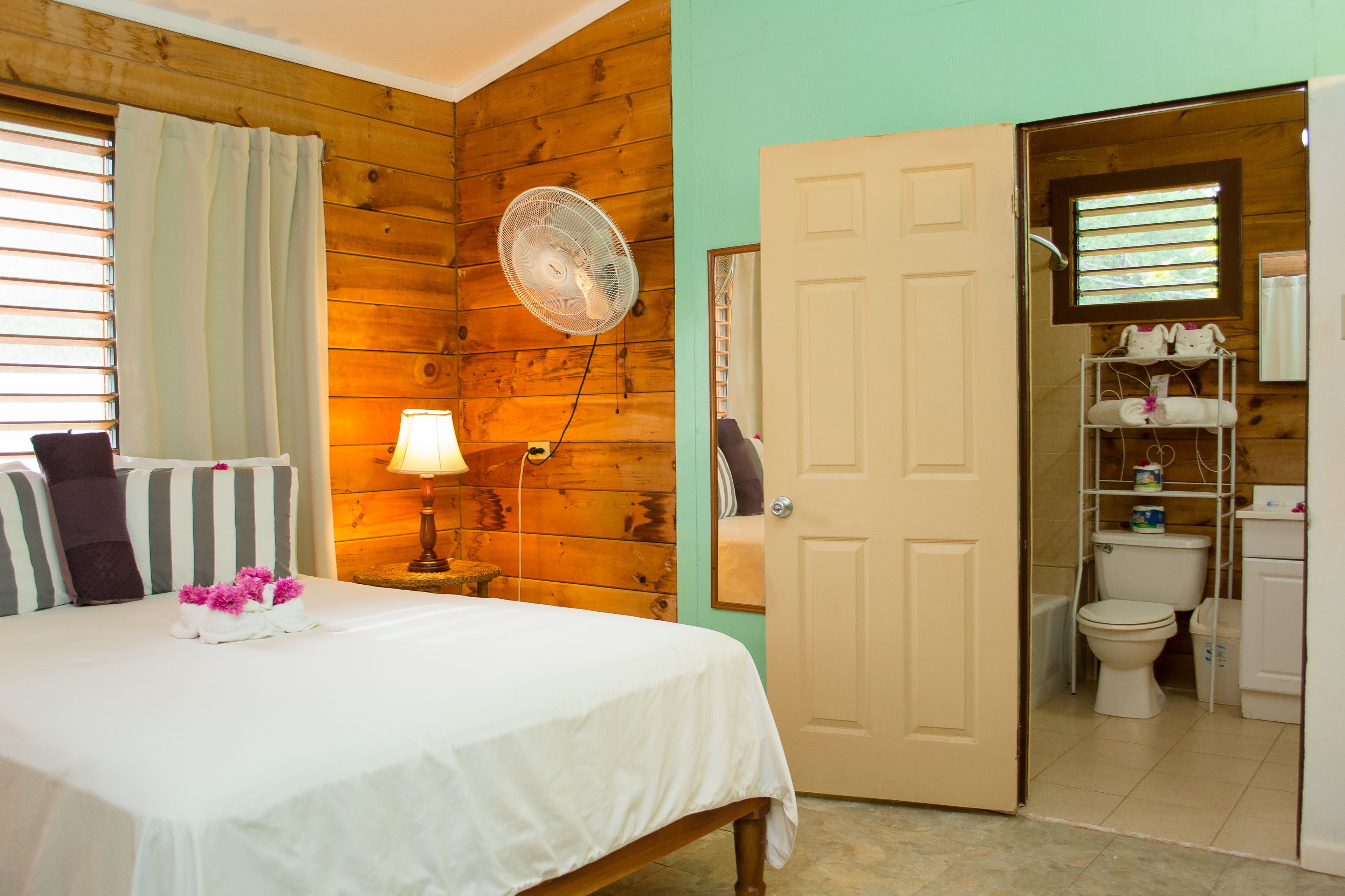 Un dormitorio con cama, ventilador de noche, lámpara y ventana con cortinas.