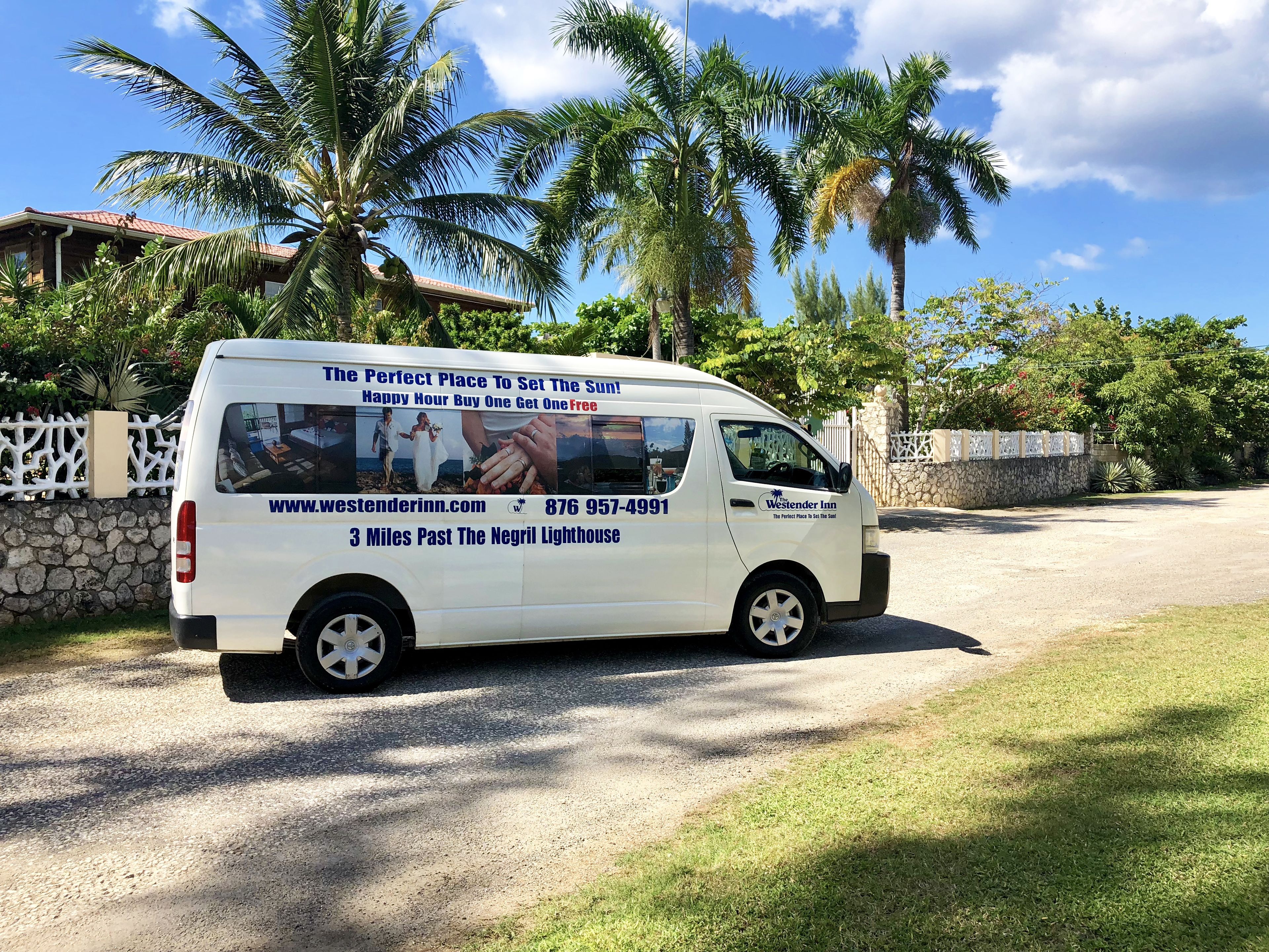 A white van parked on a gravel driveway with a sign advertising Westender Inn, located 3 miles past the Negril Lighthouse.