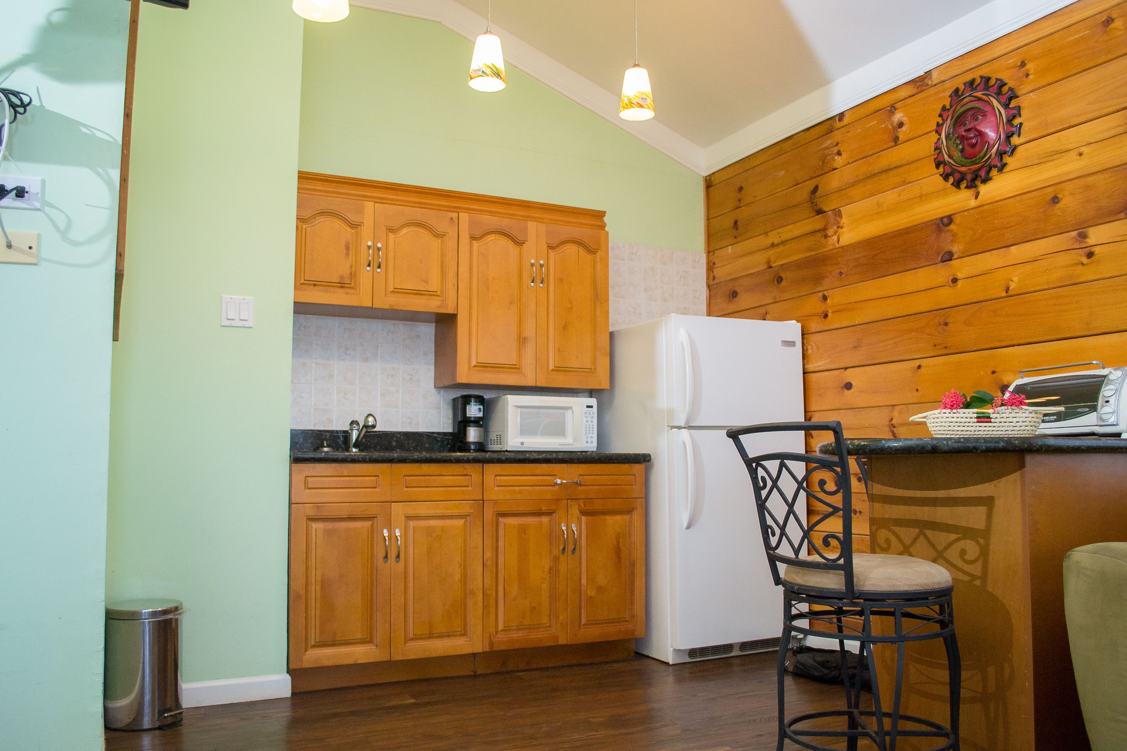 A kitchen with wooden cabinets, a microwave, a refrigerator, a sink, and a chair.