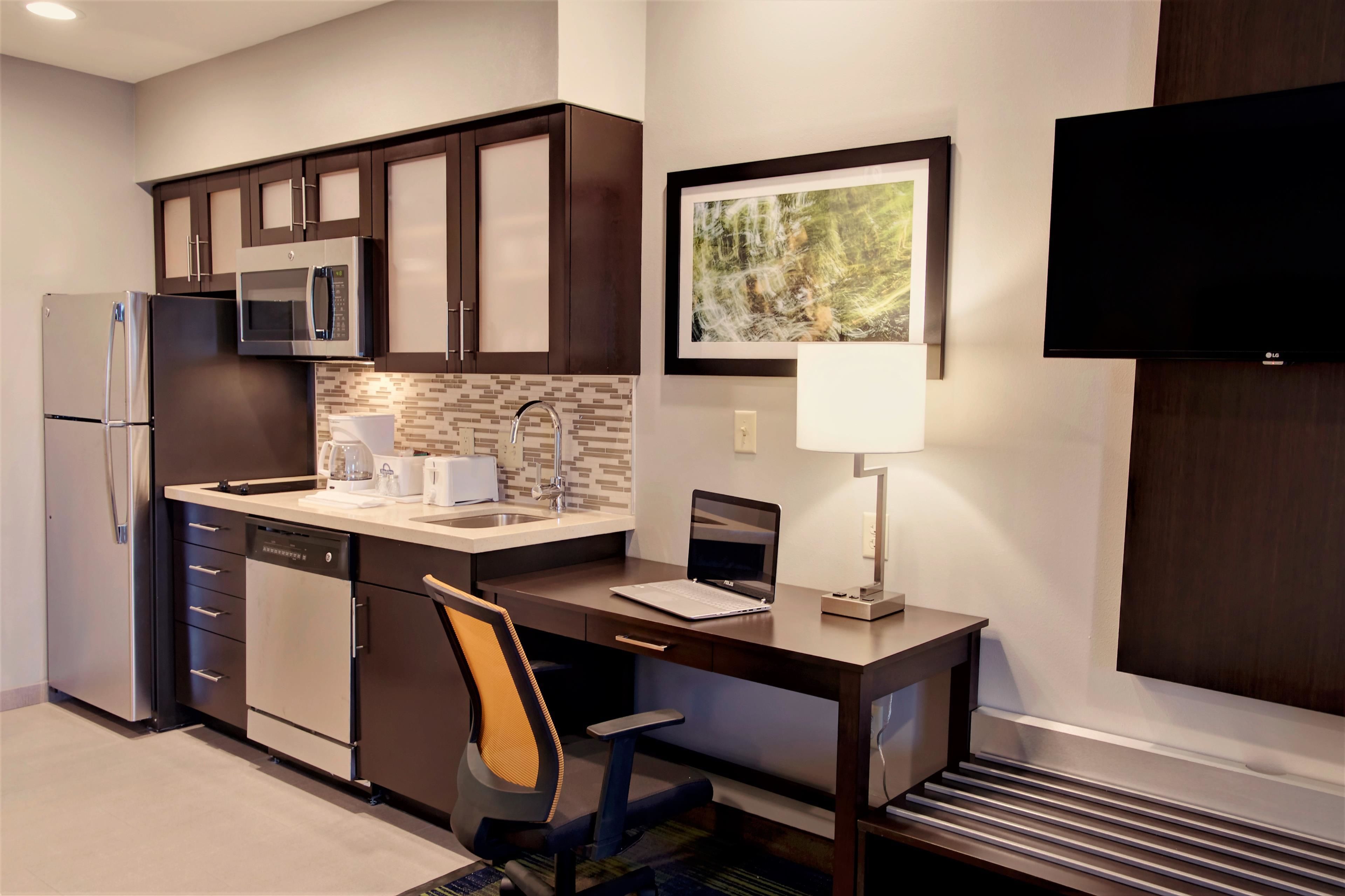 A modern kitchen with dark cabinetry, stainless steel appliances, a built-in microwave, and a laptop on the counter.