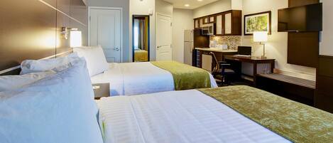 A hotel room with two beds, a kitchenette, a desk, and a TV.