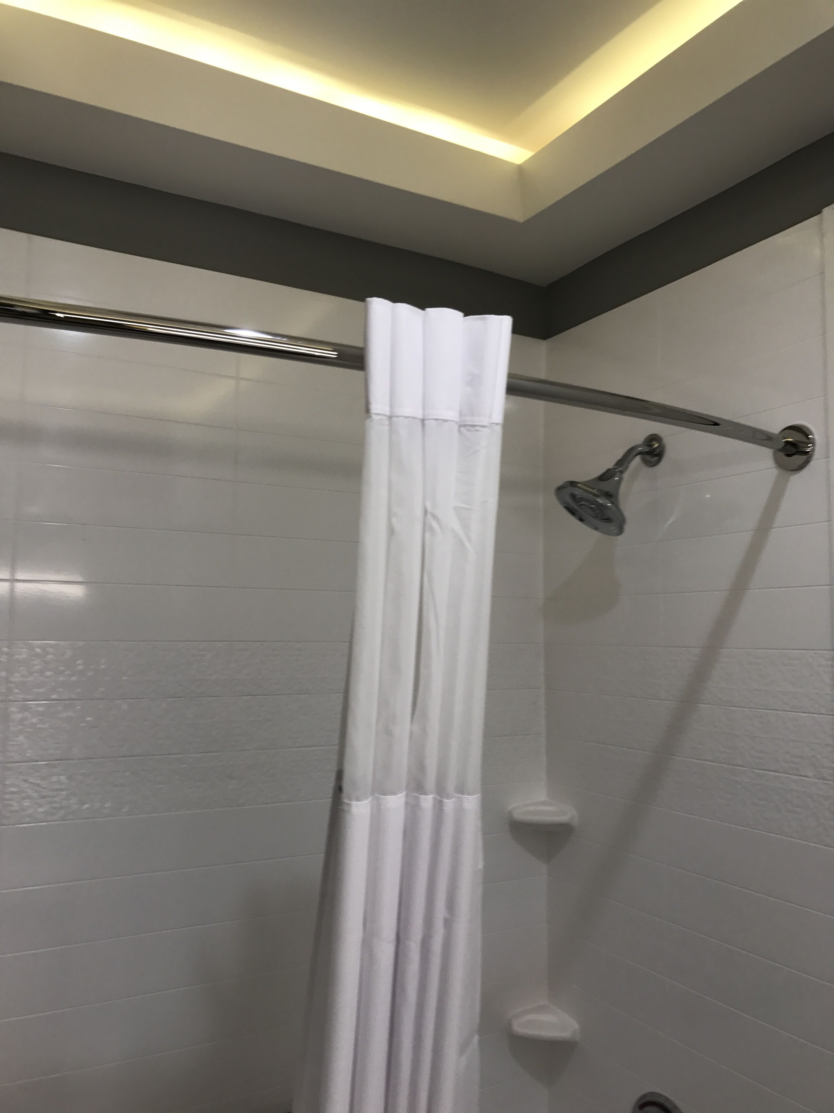 Um chuveiro com cortina branca, um chuveiro manual e um porta-toalhas fixado na parede.