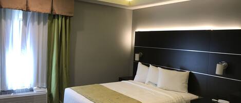 A hotel room with a bed, a nightstand, a ceiling fan, a window with curtains, and an air conditioning unit.