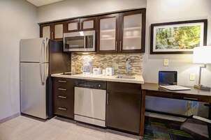 Una cocina compacta equipada con refrigerador, microondas, lavavajillas y un pequeño espacio de trabajo con una laptop.