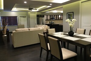 Una sala moderna con sofá y mesa de comedor, una cocina al fondo y un ventilador de techo.