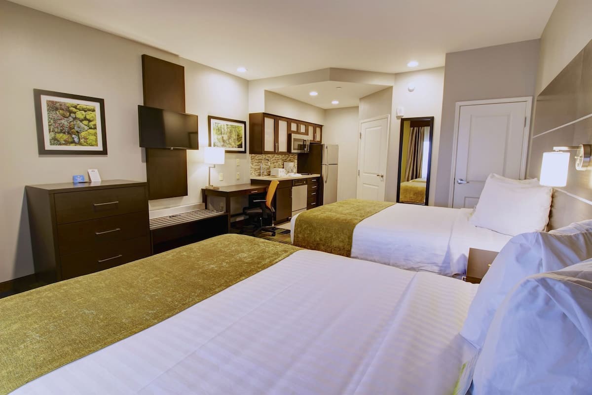 A hotel room with two beds, a desk, a chair, a TV, and a bathroom.