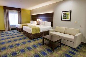 A hotel room with two beds, a sofa, a coffee table, and a painting on the wall. - Days Inn & Suites by Wyndham Port Arthur (Port Arthur)