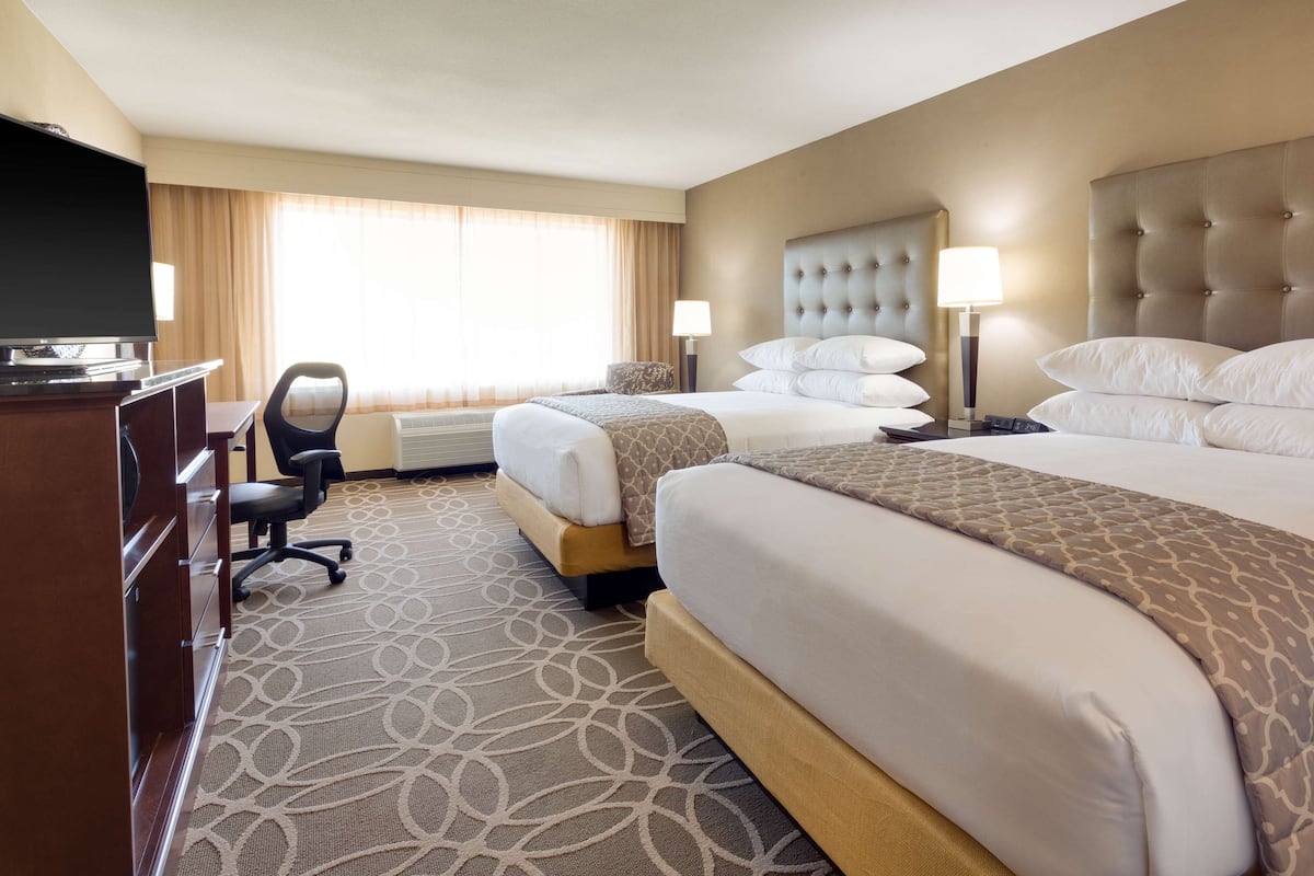A hotel room with two beds, a desk with a television, and a chair.