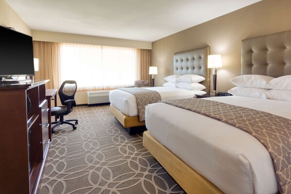 A hotel room with two beds, a desk with a television, and a chair.