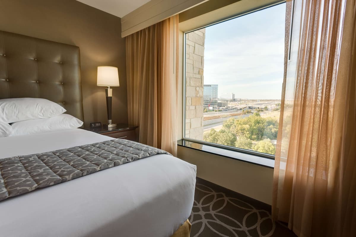 A hotel room with a large bed, a nightstand with a lamp, and a window with curtains.