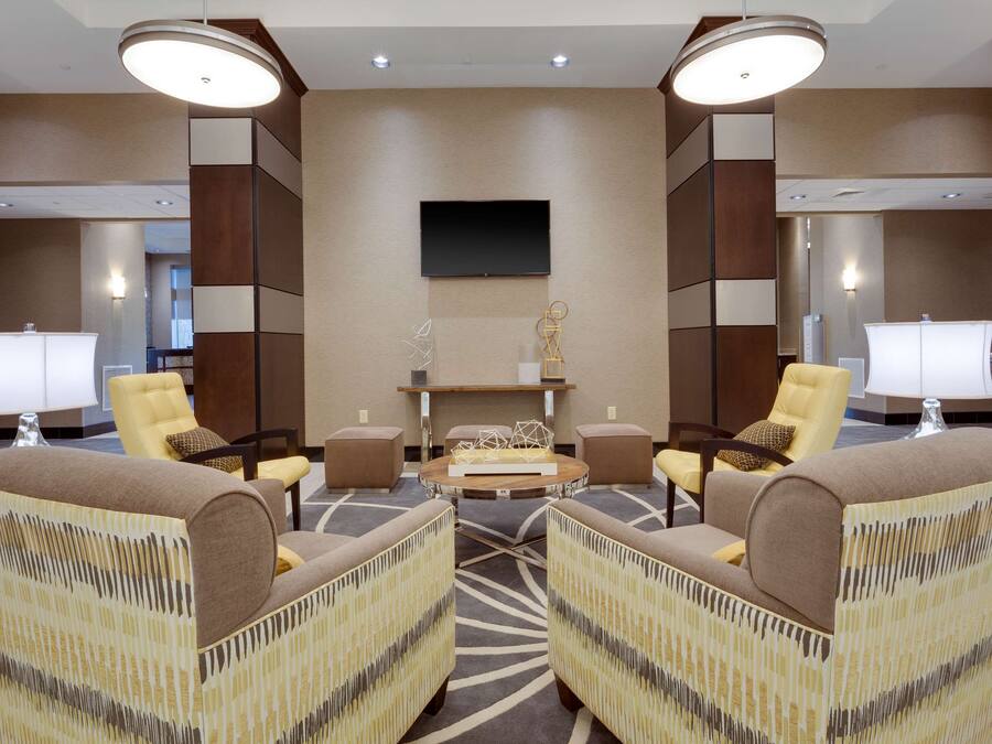 A modern lobby with a central seating area, a flat-screen TV mounted on the wall, and a reception desk with a lamp.