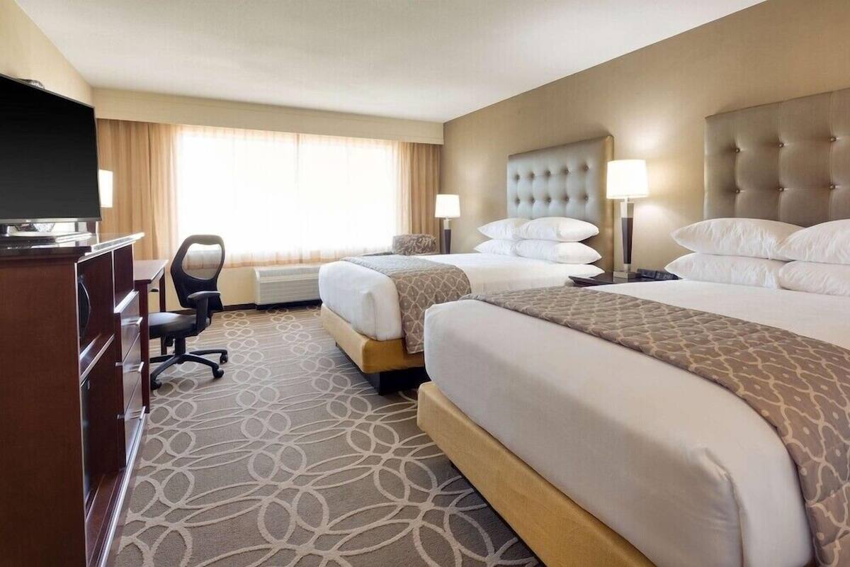 A hotel room with two beds, a desk with a TV, a chair, and a patterned carpet.
