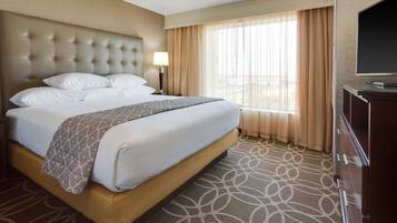 A hotel room with a large bed, a TV, and a window with curtains.