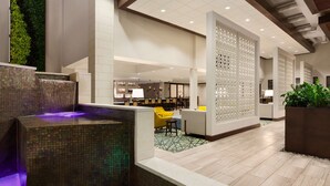 A modern hotel lobby with a central water feature, seating areas, and a reception desk.