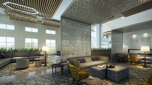 A spacious lobby with a modern design, featuring a large seating area with sofas and armchairs, a patterned carpet, and decorative ceiling panels.